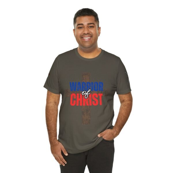 Olive green "Warrior of Christ" T-shirt featuring a rustic cross in the background with bold red, white, and blue lettering. Christian faith-based apparel for patriotic believers.