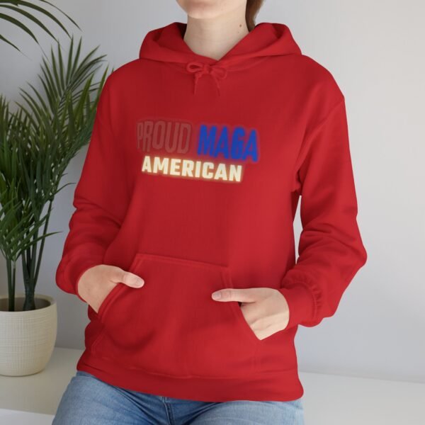 Woman wearing a Proud MAGA American hoodie in bold red, standing in a modern indoor setting. The hoodie features a patriotic design with "Proud MAGA American" text in red, white, and blue. A comfortable and stylish statement piece for conservative Americans.