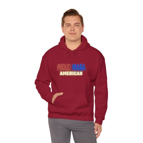 Confident man wearing a red "Proud MAGA American" hoodie, hands casually in pocket, standing against a clean white background. A bold conservative fashion statement.